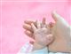 Gros plan sur fond rose une main de nourrisson tenue tendrement par une main de son parent